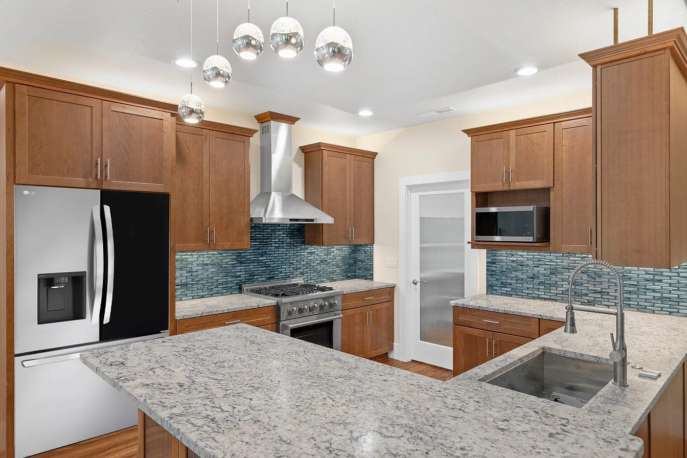 A bright custom kitchen with granite counters, glass-tile backsplash, and warm wood cabinetry